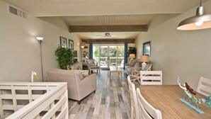 A spacious living room with a wooden floor, white furniture, and a dining table with a mermaid decoration.