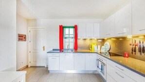 A modern kitchen with white cabinets, a central island, and a window with red curtains. - Beheizter Pool mit 2 R Apt Sea+ Parkview (Mogán)