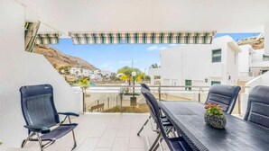 A terrace with a table and chairs, a view of a hillside, and a building in the background. - Beheizter Pool mit 2 R Apt Sea+ Parkview (Mogán)