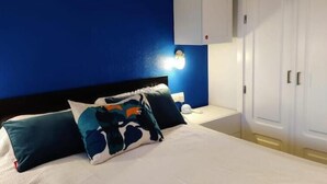 A bedroom with a bed, white cabinets, a blue accent wall, and a nightstand with a lamp. - Beheizter Pool mit 2 R Apt Sea+ Parkview (Mogán)