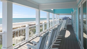 Ein überdachter Balkon mit weißen Geländern und Stühlen, mit Blick auf einen Strand.