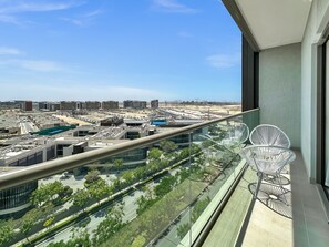 Un balcón con barandilla de vidrio que ofrece vistas a un paisaje urbano con edificios modernos y cielo despejado.