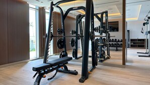 Un gimnasio moderno con varios equipos de ejercicio, incluyendo una banca de pesas y estantes para pesas.