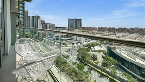 Un balcón con una silla blanca, vista de un paisaje urbano con edificios modernos y un cielo azul despejado.