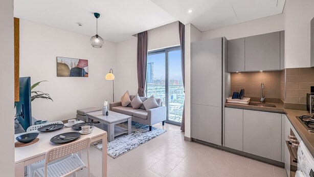 Un apartamento moderno con sala de estar, comedor y cocina. Cuenta con un gran ventanal con vista a la ciudad, un sofá, una mesa de centro y una mesa de comedor con sillas.