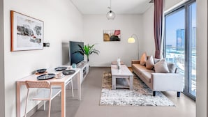 Una sala de estar moderna con comedor, sofá, televisor y un amplio ventanal con vista a la ciudad.