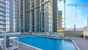 Una piscina en la azotea con sillones de descanso y vistas a un horizonte urbano y grúas de construcción.