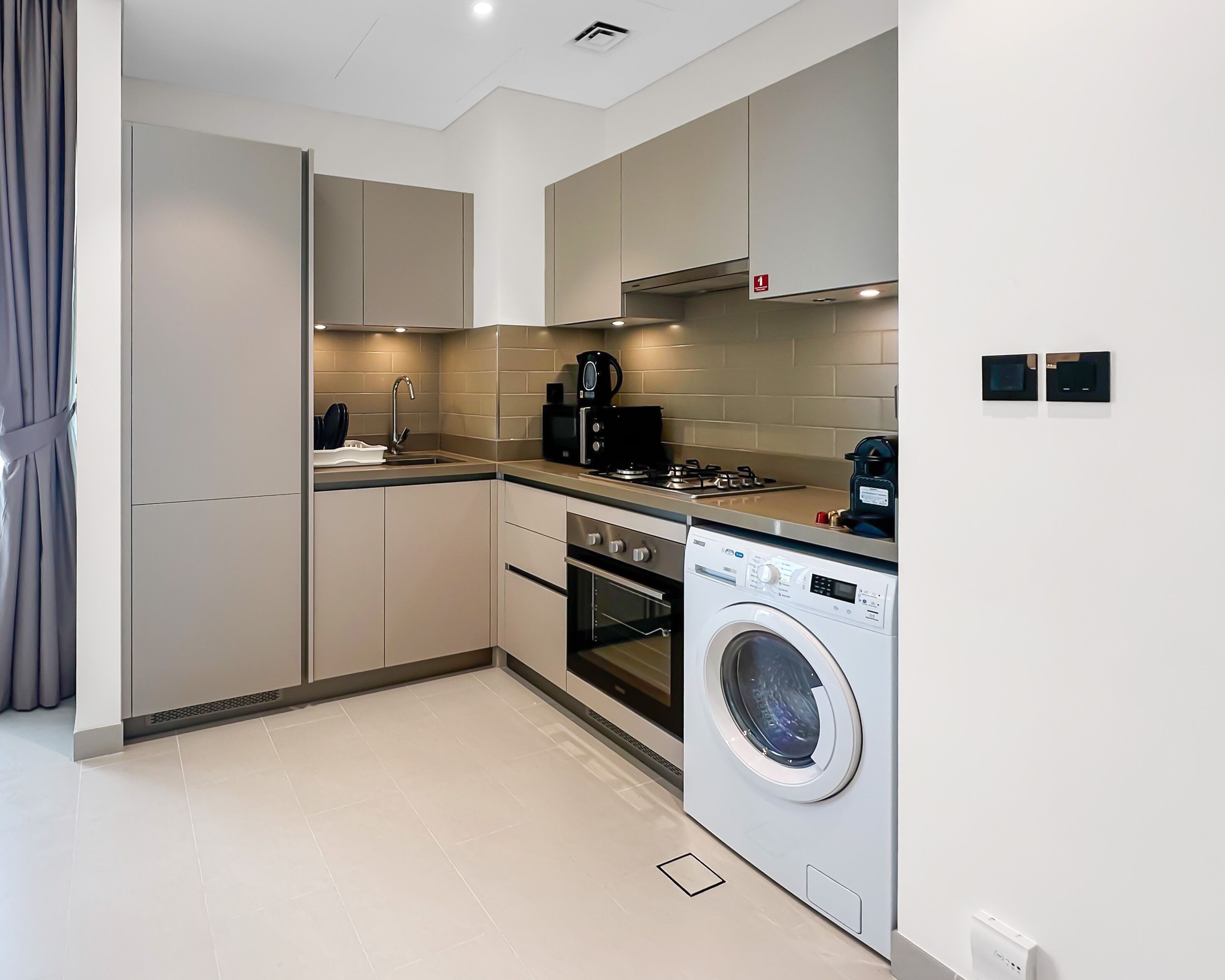 Une cuisine moderne équipée d’un lave-linge et d’un sèche-linge intégrés, d’une machine à café et d’une cuisinière à gaz.