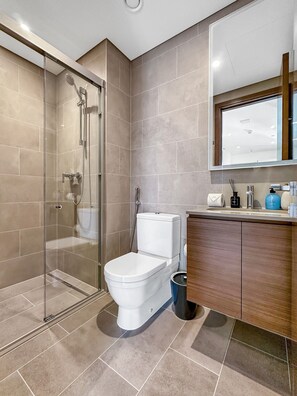 Un baño moderno con ducha de vidrio, inodoro y tocador de madera con espejo.