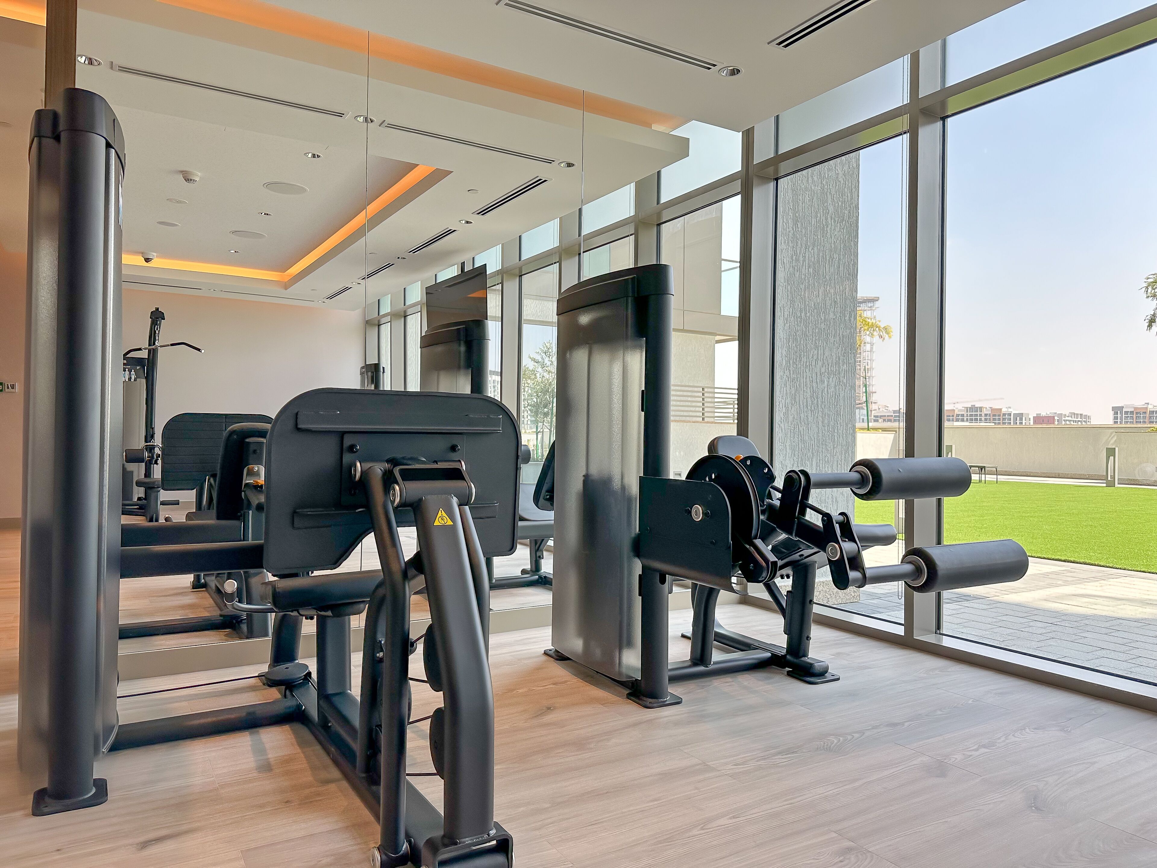 A modern gym with various exercise equipment, large windows, and a view of the outdoors.