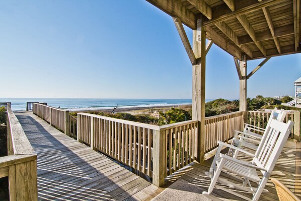 A wooden deck with a railing overlooking the ocean, white lounge chairs, and a covered area with a view of the beach. - Cross Pointe, Oceanfront House in Emerald Isle, NC! (Emerald Isle)