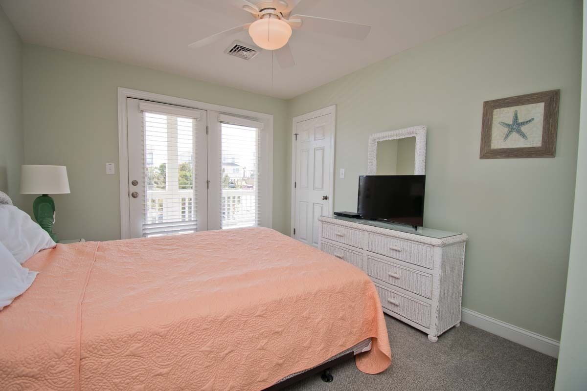Une chambre à coucher comprenant un lit, une commode, un téléviseur et un ventilateur de plafond.