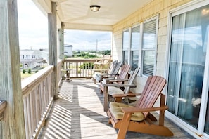 Een houten terras met een balustrade, diverse Adirondack-stoelen en uitzicht op de wijk.