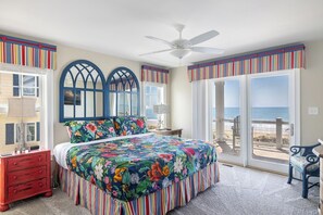 A bedroom with a large bed, a ceiling fan, a view of the beach, and a balcony with a chair. - The Nautilus, Oceanfront house in Emerald Isle, NC! (Emerald Isle)