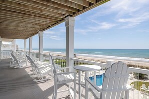 A wooden deck with white chairs and a table, overlooking a beach and a pool. - The Nautilus, Oceanfront house in Emerald Isle, NC! (Emerald Isle)