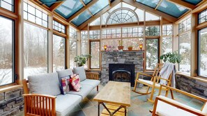 A cozy room with a stone fireplace, a sofa, a table, and wooden rocking chairs.