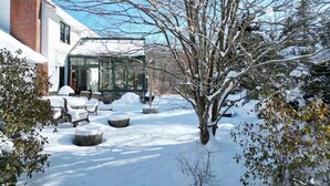 A snow-covered garden with a glass conservatory, a brick chimney, and outdoor seating.