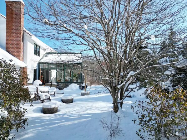 A snow-covered garden with a glass conservatory, a brick chimney, and outdoor seating.