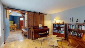 A cozy living room with a piano, a wooden bookshelf, a dining table, and a bench.