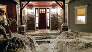 A snow-covered pathway leading to a house with a stone facade and a wooden door.