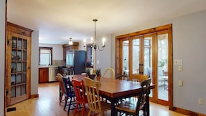 Un espace repas avec une table et des chaises en bois, un lustre et une vue dégagée grâce à de grandes portes vitrées.