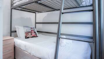 Una cama litera con estructura metálica, ropa de cama blanca y un almohadón con diseño de faro.