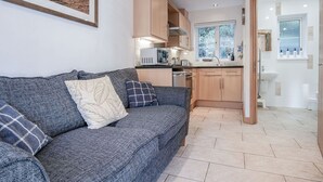 Un salon moderne avec un canapé gris et un coin cuisine doté de meubles en bois et d’une fenêtre.