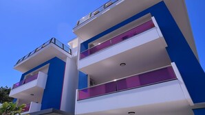 Un immeuble moderne à plusieurs étages, doté de balcons, se dressant sous un ciel d’un bleu éclatant.