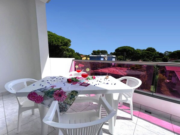 A balcony with a table set for two, featuring a white tablecloth, floral decorations, and a glass of red drink.