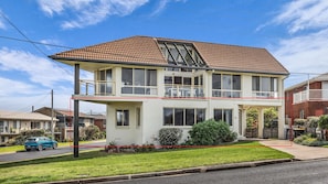 A two-story residential building with a balcony, a front porch, and a well-maintained lawn.