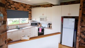 A compact kitchen with white cabinets, a microwave, stove, and a refrigerator. - Beachview 2 - Scenic Drive 33 (Bermagui)
