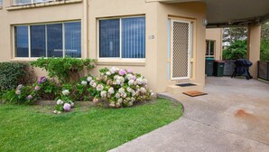 A residential building with a well-maintained garden, a covered patio area, and a visible trash bin. - Beachview 2 - Scenic Drive 33 (Bermagui)