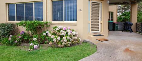 A residential building with a well-maintained garden, a covered patio area, and a visible trash bin.