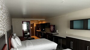 Ein Hotelzimmer mit zwei Betten, einer Küchenzeile, einem Badezimmer und einem an der Wand befestigten Fernseher.