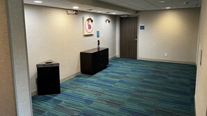 Ein Hotelzimmer mit blauem Teppich, einem Schreibtisch mit Papierkorb, einer Tür und einer Wandleuchte.