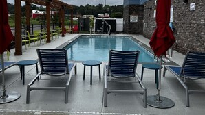 Ein Poolbereich mit Liegestühlen und Sonnenschirmen, eine Steinmauer und ein Gebäude mit mehreren Fenstern.