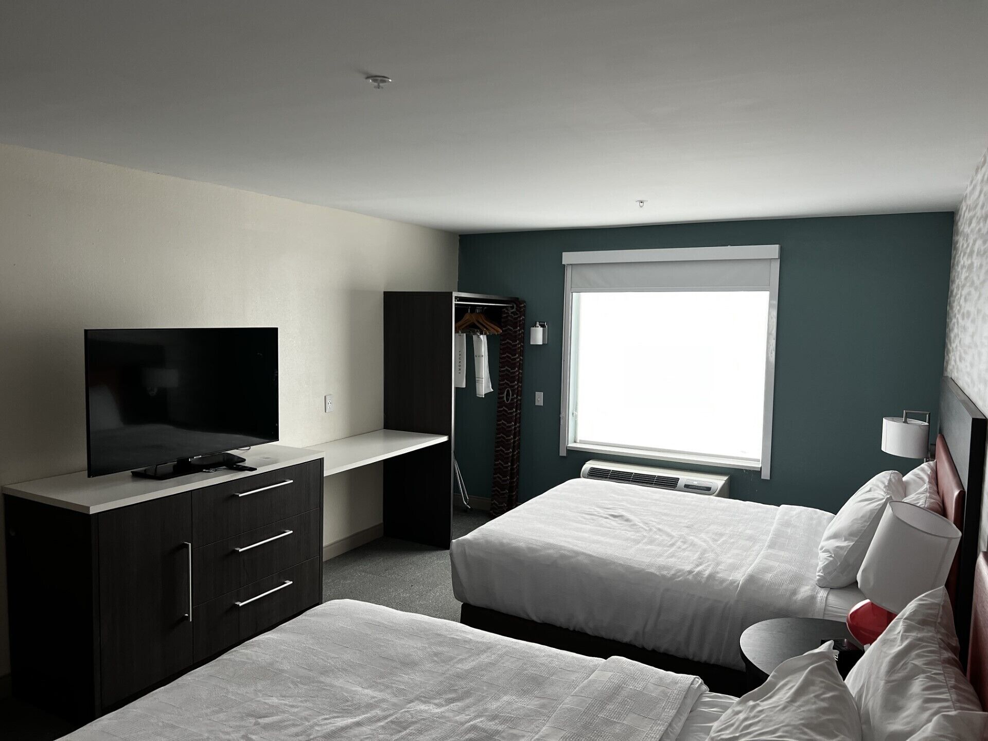 A hotel room with a TV, wardrobe, two beds, a window, and a bedside table.
