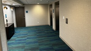 Ein Hotelgang mit blauem Teppich, einer Rezeption und zwei Aufzügen.