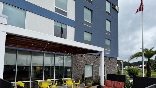 Ein modernes Hotel mit Außenbestuhlung, einer überdachten Terrasse und einer Fahnenstange.