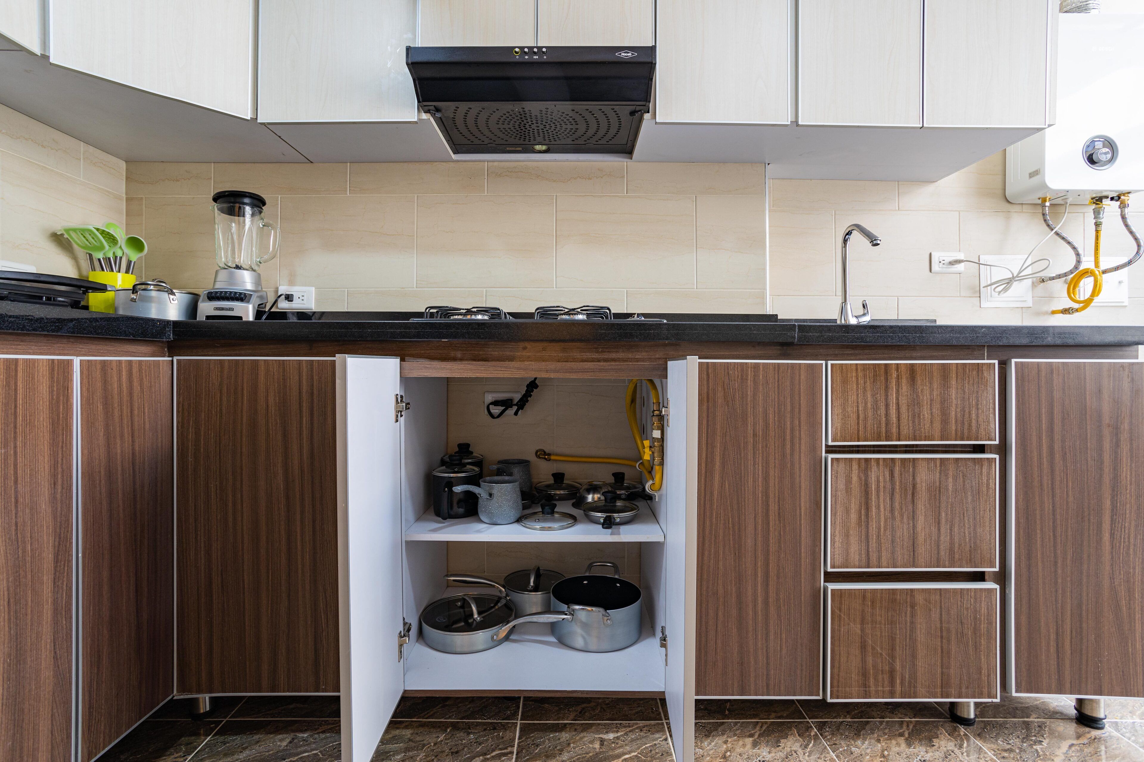 A kitchen with wooden cabinets, a black range hood, a countertop with a blender, and a water filtration system.