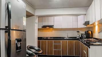 Una cocina moderna con refrigerador de acero inoxidable, gabinetes de madera, estufa a gas y cafetera.