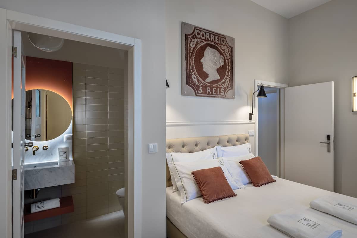 A hotel room with a bed, a bathroom with a mirror, and a wall-mounted sign.