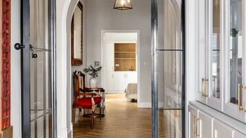 A modern interior with a wooden herringbone floor, glass doors leading to a dining area with a red chair and table, and white cabinets with gold handles.