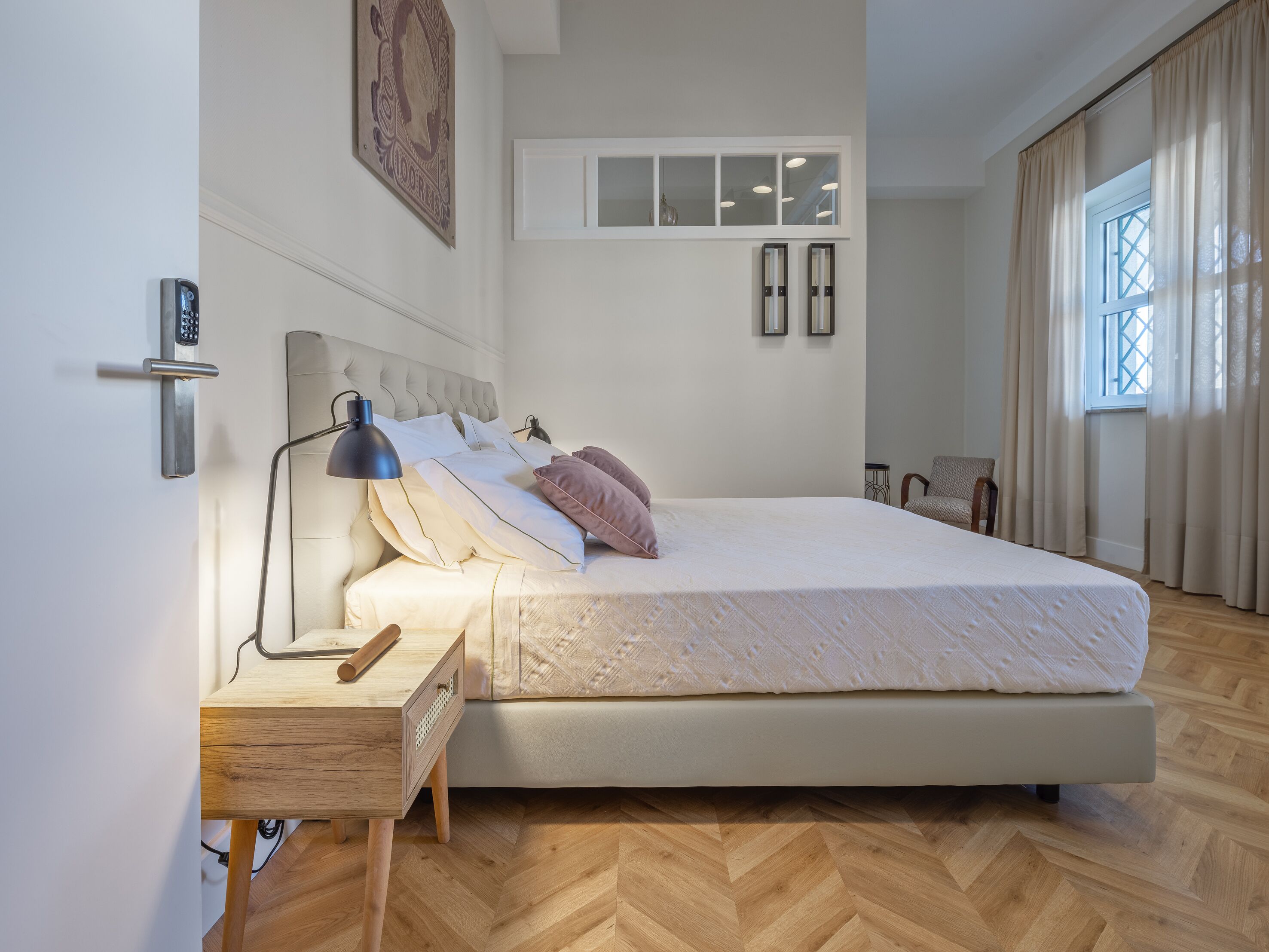 A bedroom with a large bed, bedside table, lamp, and a wall-mounted light fixture.