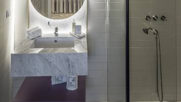 Un baño moderno con un lavabo de mármol, un espejo grande y una ducha con mampara de vidrio.