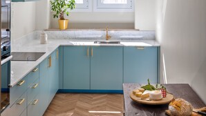 A modern kitchen with teal cabinets, a marble countertop, and a wooden dining table with bread. - Casa dos Correios (Vila Real)