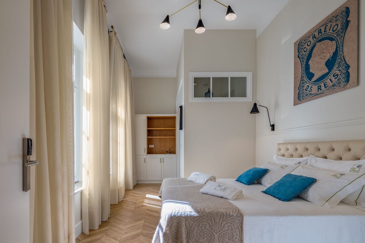 A bedroom with a bed, curtains, a wall-mounted light, a window, and a wall decoration.