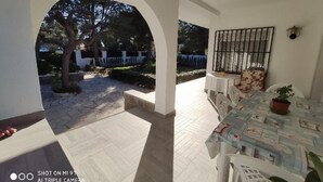 An outdoor patio area with a table and chairs, a potted plant, and a view of a garden with trees and a white fence. - SAONA VILLAS (VN CUAD): villa for 8 people, private pool, wifi (Tres Calas)