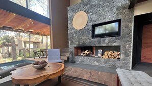 A modern living room with a stone fireplace, a flat-screen TV, and a large window overlooking a pool. - Vacation house with private pool and hottub (Valle de Bravo)
