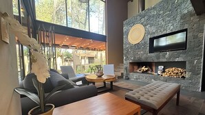 A modern living room with a stone fireplace, comfortable seating, and a large window overlooking a garden. - Vacation house with private pool and hottub (Valle de Bravo)